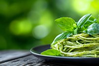 Fresh pasta with homemade basil pesto sauce garnished with green leaves on dark plate against blurred natural background, close up view of Italian cuisine.
