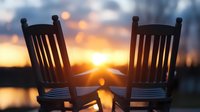 Two wooden rocking chairs silhouetted against golden sunset over water, creating romantic peaceful atmosphere for relationship and retirement concepts.