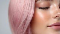Close up portrait of young woman with pink pastel hair, closed eyes and natural makeup showing flawless skin texture and gentle smile on light background.