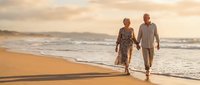 Senior couple walking hand in hand on beach at sunset during romantic vacation getaway enjoying golden hour light and ocean waves.