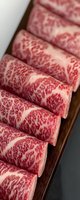 Fresh marbled beef slices arranged in row showing distinctive white fat patterns against red meat on dark wooden surface, close-up macro photography.