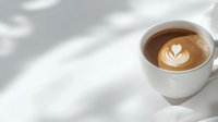 Creamy latte art heart pattern in white ceramic cup on light surface with soft natural window shadows creating minimalist composition for cafe menu design.