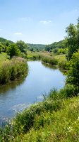 Scenic river flowing through lush green valley with dense vegetation, rolling hills, and clear blue sky. Ideal for nature, landscape, and environmental design projects.