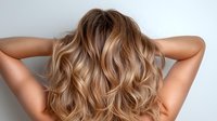 Blonde wavy hair from behind showing modern balayage technique with natural highlights and soft curls styled for salon advertising and beauty industry.