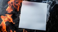 Blank white paper with bright orange flames burning at edges against dark background, dramatic lighting creates intense contrast and smoky atmosphere.