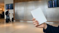 Person holding blank white card in modern airport terminal with departure boards and travelers in background.