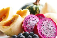 Fresh cut watermelon radish with vibrant pink flesh, cantaloupe slices and blueberries arranged on white surface, macro food photography showing texture and detail.