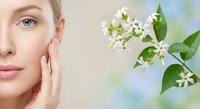 Young Caucasian woman touching face with white jasmine flowers for natural skincare and beauty treatment concept on soft blurred background.
