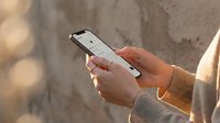 Woman hands holding smartphone with mobile app interface in warm sunlight against textured wall background for digital communication and technology concepts.