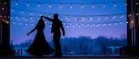 Romantic couple dancing silhouettes under string lights at twilight evening celebration with blue sky background for wedding anniversary events.