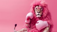 Male lion with pink mane wearing boxing gloves against pink background, creative concept combining strength and playfulness, surreal animal portrait.