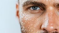 Close up portrait of male face with water drops on skin showing half of face with blue eye and eyebrow in macro photography on light background.