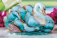 Elegant swan brooch in turquoise and gold tones with crystal embellishments, featuring delicate enamel work and intricate details against blurred floral background.
