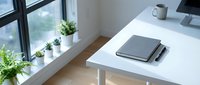 Clean minimalist workspace with notebook and pen on white desk near window with small potted plants creating productive home office environment.