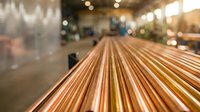 Copper pipes arranged in parallel rows inside industrial warehouse facility with blurred background lighting and manufacturing equipment.