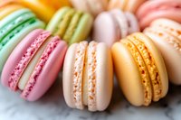 Colorful French macarons in pastel shades of pink, yellow, green, and orange arranged in row on marble surface, showing detailed texture of meringue cookies.