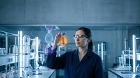 Female scientist in lab coat examining orange liquid sample with DNA helix hologram projection in modern laboratory for biotechnology research and development.