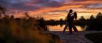Romantic couple silhouette embracing at sunset by lake with dramatic orange sky reflecting on water creating peaceful evening atmosphere for love concepts.