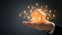 Real estate investment concept with businessman hand holding glowing house model surrounded by floating currency symbols for financial planning.