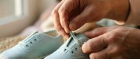 Senior woman hands tying white canvas sneakers with shoelaces in bright natural light for comfortable walking and daily activities.