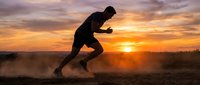Silhouetted male athlete sprinting at sunrise with dramatic golden sky and dust clouds, capturing dynamic motion and endurance training for fitness and sports marketing.