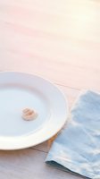 Minimalist coastal table setting with white ceramic plate, small seashell, and blue linen napkin on light wooden surface for dining and hospitality design.