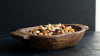 Wooden bowl filled with mixed nuts and dried fruits on dark surface for healthy snacking and cooking ingredients.