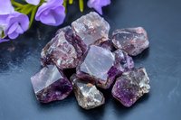 Raw amethyst crystal chunks on dark slate background with purple flowers, displaying natural mineral formation and metaphysical properties for wellness and decoration.
