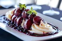 Fresh poached pears in red wine sauce served on vanilla cream with mint garnish, elegant plated dessert on white ceramic dish against dark background.