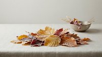 Autumn leaves scattered on linen tablecloth with wooden bowl, perfect for seasonal home decor, thanksgiving table setting and fall crafting projects.