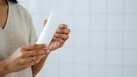 Woman with dark skin tone holding blank white paper or document against neutral background for business, communication, or presentation purposes.