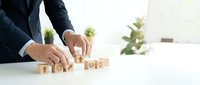 Businessman arranging wooden blocks with year 2024 numbers on white desk in modern office environment for planning and goal setting.