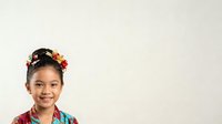 Young Asian girl with long dark hair adorned with colorful flower crown, wearing vibrant traditional clothing, smiling at camera against neutral background for portrait and cultural celebration designs.