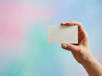 Hand holding blank cream business card against soft pastel gradient background in pink, blue and turquoise tones for branding and corporate identity mockup.