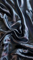 Luxurious black silk fabric with smooth waves and folds creating elegant abstract pattern. Subtle pink and blue reflections add depth to silky textile surface.