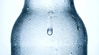 Closeup of cold water droplets condensing on frosted glass bottle surface with single drip falling, isolated on white background for beverage, refreshment and hydration design projects.