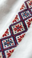 Traditional folk embroidery with red, blue, and gold geometric floral cross-stitch pattern on white linen fabric, ethnic textile craft detail.