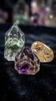Collection of polished healing crystals including green fluorite tower, purple amethyst and golden rutilated quartz on dark surface for meditation and wellness.