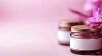 Cosmetic cream jars with pink flowers on soft pink background, selective focus. Luxury skincare and beauty product packaging for spa and wellness.