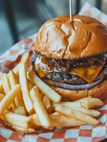 Juicy cheeseburger with melted cheese, caramelized onions and beef patty served with crispy french fries on checkered paper in casual dining setting.