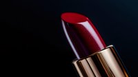 Deep red lipstick with metallic gold case against dark background, dramatic lighting highlights glossy texture and luxurious finish, makeup artistry and cosmetics.