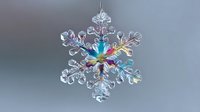 Crystal snowflake ornament with rainbow iridescent center hanging against gray background, showcasing delicate glass craftsmanship for holiday decor.