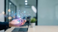 Caucasian male professional holding glowing digital network icons and data symbols in palm, representing cloud computing, cybersecurity, and technology innovation in modern office workspace.