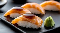 Fresh salmon nigiri sushi pieces with soy sauce glaze arranged on black slate plate with wasabi paste, traditional Japanese cuisine served at restaurant.