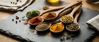 Colorful spices and herbs arranged in wooden spoons on dark slate surface for cooking and seasoning culinary ingredients kitchen preparation.