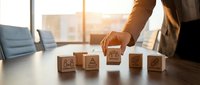 Businessperson arranging wooden blocks with business strategy icons on a conference table, symbolizing teamwork, planning, and corporate growth.