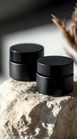 Black cosmetic jars on natural stone with dried flowers in soft lighting, minimalist spa composition for skincare and beauty product presentation.