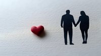 Minimalist paper cutout silhouette of loving couple holding hands with red heart shape, symbolizing romance and relationship on white textured background.