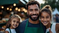 Mixed race family at farmers market stand, father in green apron with two smiling daughters against blurred bokeh lights background, authentic lifestyle portrait.