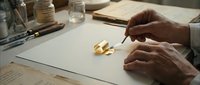 Elderly male craftsman carefully working on a shiny gold ring with precision tools at a workshop desk, showcasing fine jewelry craftsmanship.